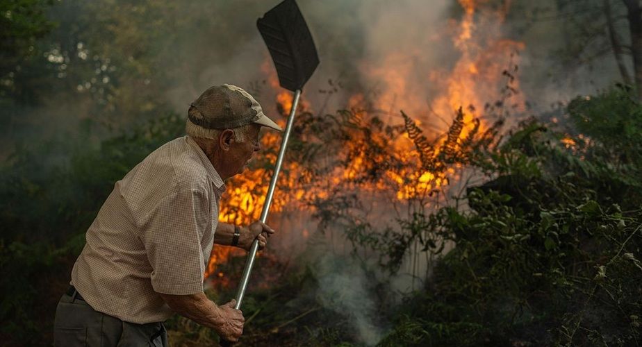 A man beats back flames with a fire beater amid smoke